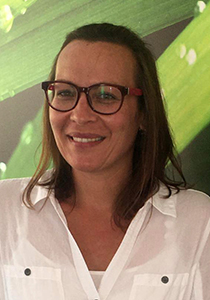 Ein Porträt zeigt Anita, ein lächelndes Teammitglied mit dunklen Haaren und einer Brille. Sie trägt ein weißes Hemd mit Kragen.