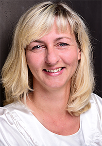 Eine fröhliche, blondhaarige Frau, das Teammitglied Doreen, blickt lächelnd direkt in die Kamera. Sie trägt schulterlanges Haar und ein weißes Oberteil.